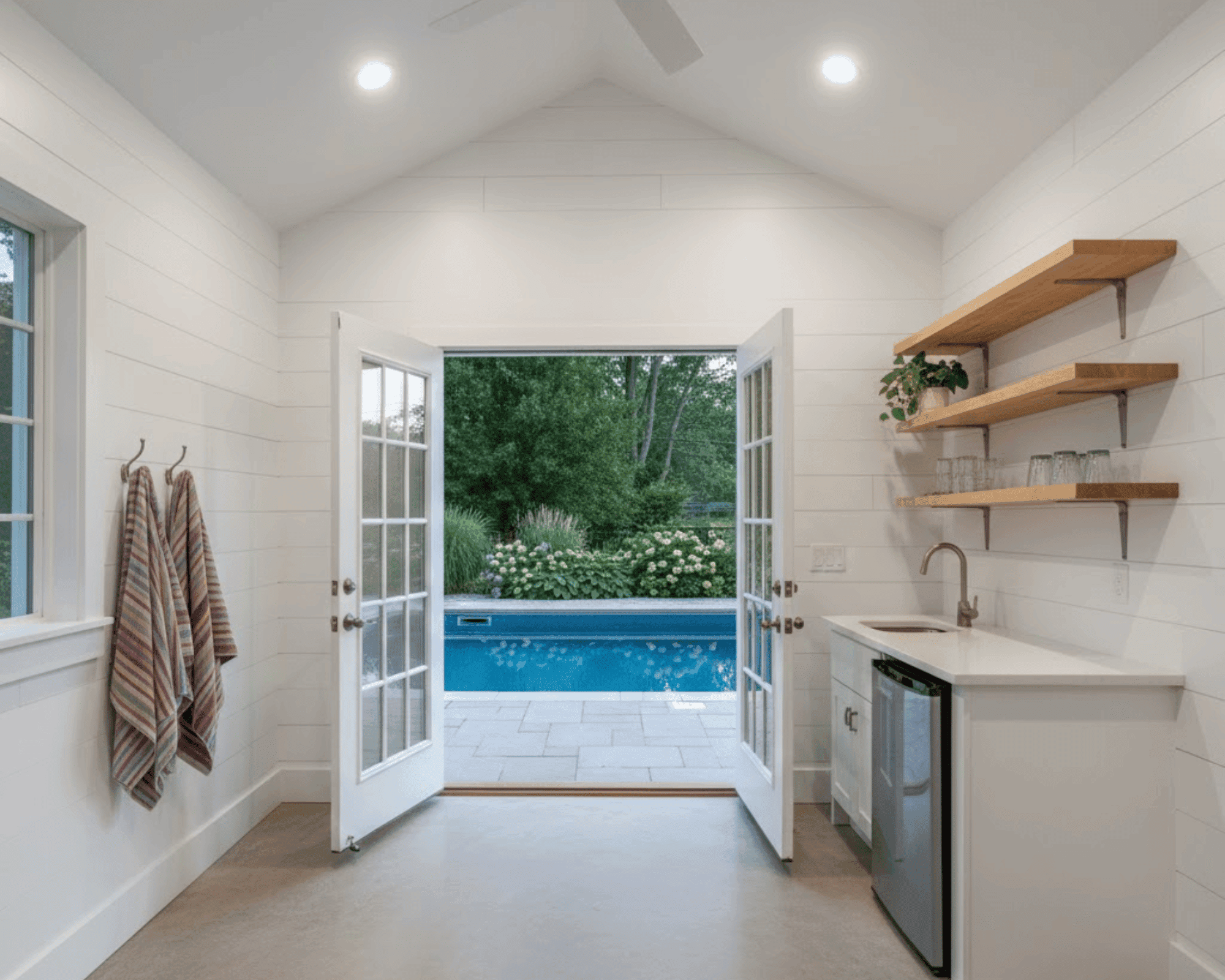 Pool house interior with kitchenette and French doors opening to pool